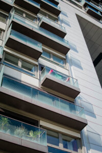 Blick-nach-oben-an-hauswand-mit-balkonen-weiss-tuerkis-glasbruestung-auf-einem-balkon-mittig-steht-waeschestaender-mit-pinker-kleidung