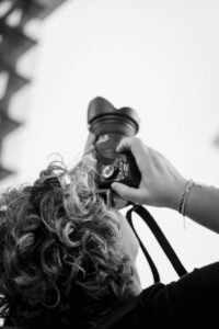 frau-mit-spiegelreflexkamera-fotografiert-an-hauswand-nach-oben-detailaufnahme-von-fotografin-und-kamera-locken-schwarzweiss