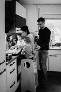 Schwarz-Weiß-Aufnahme einerFamilie beim gemeinsamen Belegen der Pizza in einer hellen, modernen Küche.