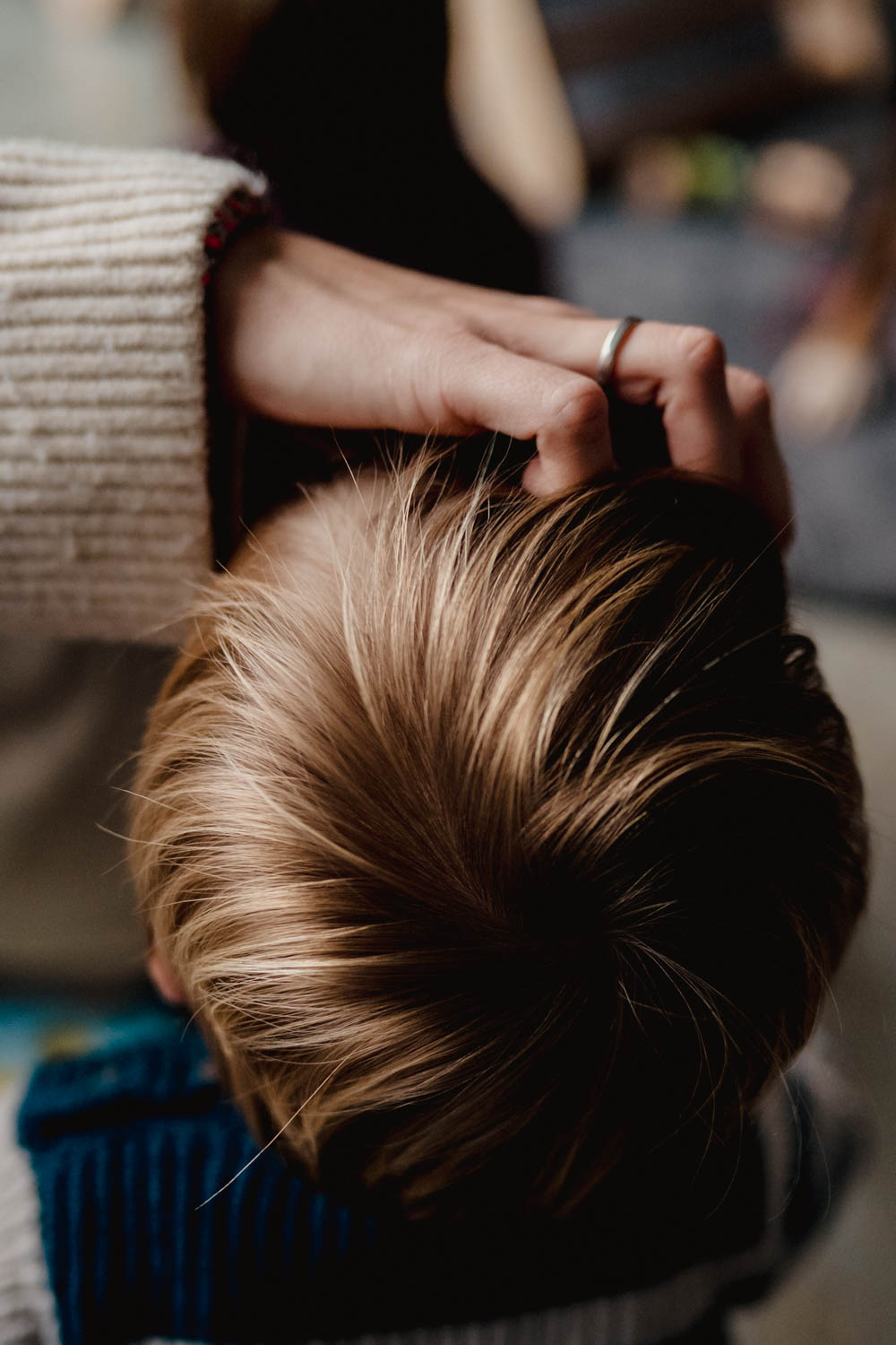 Nahaufnahme der Hand einer erwachsenen Person, die sanft durch das helle, goldbraune Haar eines Kindes streicht.